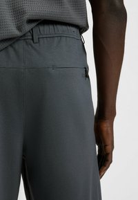 Grijze sportbroek met elastische tailleband, uitgerust met een ritszak, een gladde stoffen textuur en een tonale logodetail op de zijkant.