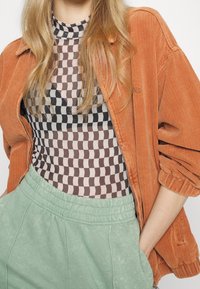 Kurtka z kordury w kolorze rdzy, noszona na topie w brązowo-czarną kratkę, zestawiona z miętowozielonymi dresami z elastycznym pasem.