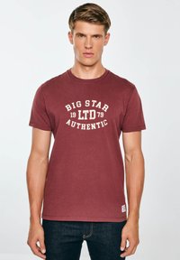 Bordo spalvos apvalaus kaklo marškinėliai, pagaminti iš minkštos medžiagos, su balta spausdinta užrašu „BIG STAR 19 LTD 79 AUTHENTIC“, esančiu centro krūtinėje.