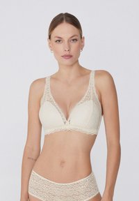 Bralette de encaje en un suave color crema con escote pronunciado, tirantes anchos de encaje y bordes festoneados, combinado con braguitas de encaje a juego.