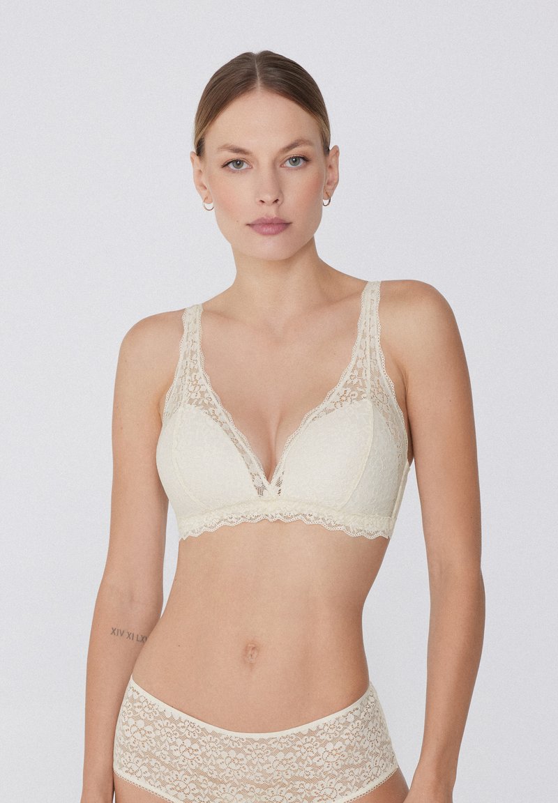 Bralette de encaje en un suave color crema con escote pronunciado, tirantes anchos de encaje y bordes festoneados, combinado con braguitas de encaje a juego.