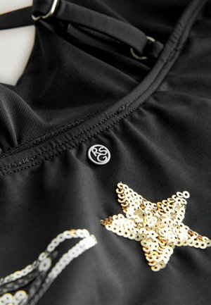 Black fabric featuring a gold sequin star design and a silver logo button. Detailed stitching and adjustable straps are also visible.