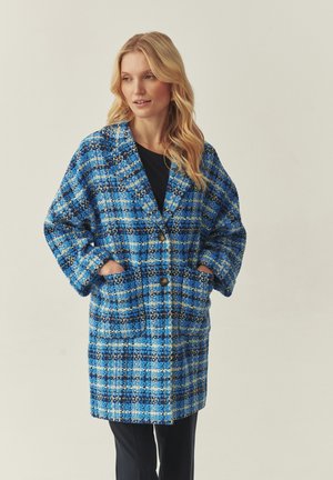 Blauer und schwarzer karierter Mantel mit lockerem Schnitt, großen Taschen und Knopfverschluss, aus strukturiertem Stoff mit weiten Ärmeln.