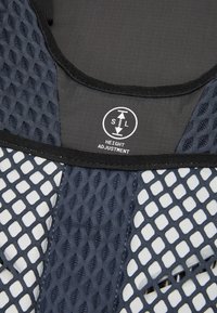 Síťový postroj s nastavitelnou výškou v námořnické modré a černé barvě. Texturovaná síťovina se znakem indikujícím nastavení výšky. Hladký materiál na zadní straně.