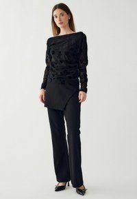 Fekete, hosszú ujjas felső virágmintával, fekete, szabott nadrággal, aszimmetrikus betéttel párosítva. A megjelenést fekete, hegyes orrú cipők zárják le.