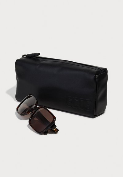 Black zippered pouch made of smooth material, paired with dark tortoiseshell sunglasses featuring square frames and brown lenses.