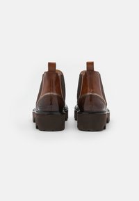 Stivali ankle in pelle marrone con pannelli laterali elasticizzati, dettagli decorati e suole in gomma spesse. Presenta un tassello sul retro.