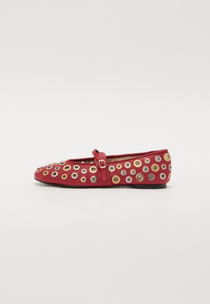 Ballerine en cuir rouge avec une lanière, arborant plusieurs œillets métalliques de teintes argentées et dorées disposés autour de l'empeigne.