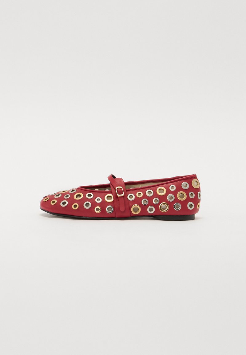 Ballerine en cuir rouge avec une lanière, arborant plusieurs œillets métalliques de teintes argentées et dorées disposés autour de l'empeigne.