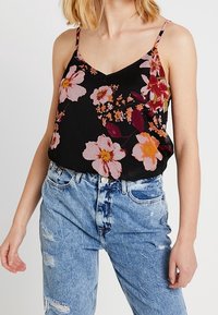 Svart blommig camisole med rosa och orange blommor, tunna band, V-ringning och en lös passform, i kombination med slitna ljusblå jeans.