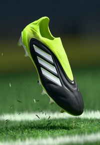 Black and neon yellow soccer cleat with a textured upper, three white stripes, and a streamlined design. Spikes visible on the sole.