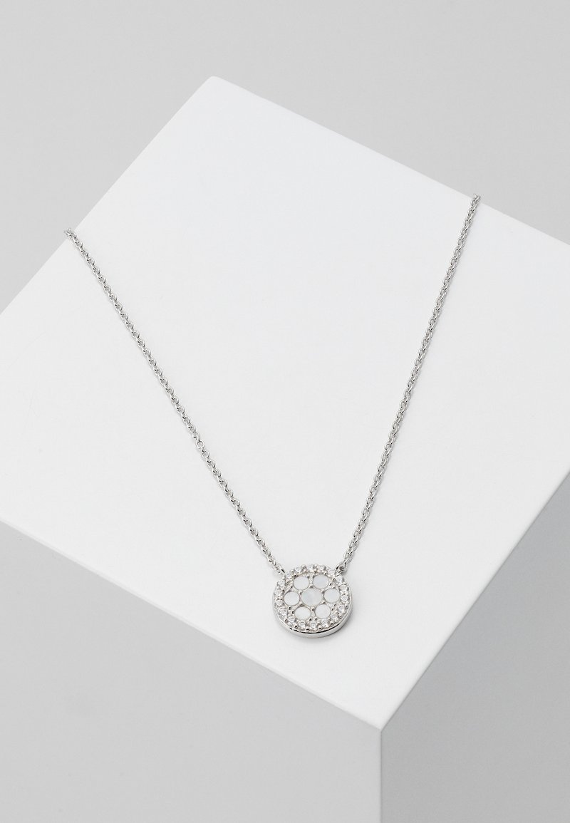 Silver halsband med cirkulär medaljong, prydd med glittrande stenar, på en fin kedja. Vit och metallisk färgpalett.