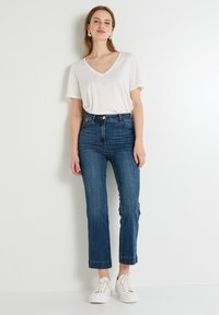 Camiseta blanca de cuello en V combinada con jeans de pierna recta de talle alto en azul oscuro, con los puños doblados, llevados con zapatillas de plataforma blancas.