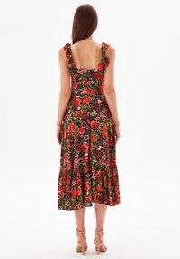 Blumenkleid in Midi-Länge mit schwarzem Grundton, versehen mit einem roten Obstprint und grünen Blättern, Rüsche an den Schulterträgern und einem stufigen Saum.