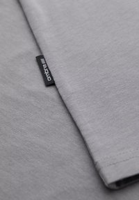 Tessuto di t-shirt grigio, texture morbida, vista ravvicinata che mostra un'etichetta con il marchio "ombre" e dettagli della cucitura del bordo della manica.