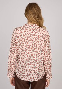 Chemise à boutons en tissu crème clair avec un motif paisley répété en rouille. Comprend un col et des manches longues avec des poignets à boutons.