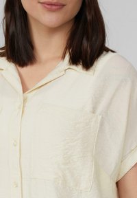 Lichtgele blouse met knopen, met een relaxte pasvorm, zachte textuur, korte mouwen en twee voorkruiszakken, met een subtiel gekreukt patroon.