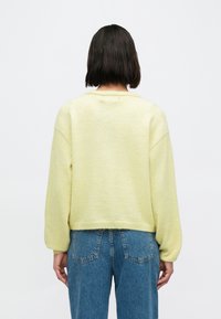 Kollane, pehme tekstuuriga džempr, millel on laskuvad õlad ja lõdvestunud istuvus, ümara kaelusega ja soonikuga ääris. Kandmiseks kombineeritud kõrge vöökohaga teksapükstega.