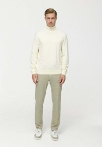 Krém színű garbó pulóver texturált, világos zöld nadrággal párosítva. A modellen fehér sportcipő van. Egyszerű design, testhez simuló szabással.