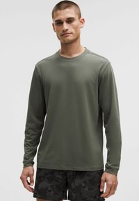 Camicia a maniche lunghe verde oliva in un tessuto leggero e liscio. Presenta un colletto rotondo e cuciture minime per un design pulito.
