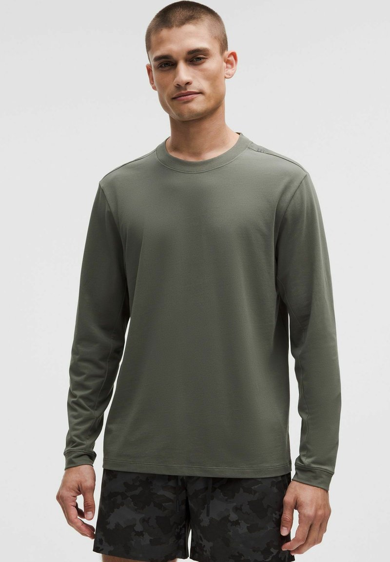 Camicia a maniche lunghe verde oliva in un tessuto leggero e liscio. Presenta un colletto rotondo e cuciture minime per un design pulito.