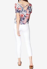 Blommönstrad topp i röd och blå nyanser, med korta ärmar och ett korsat ryggdesign. Matchad med vita tajta byxor och sandaler.