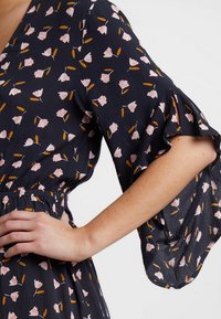 Blommig klänning med marinblå bakgrund, prydd med rosa blommor och gula detaljer. Designen har breda, volangärmar och resårmidja.