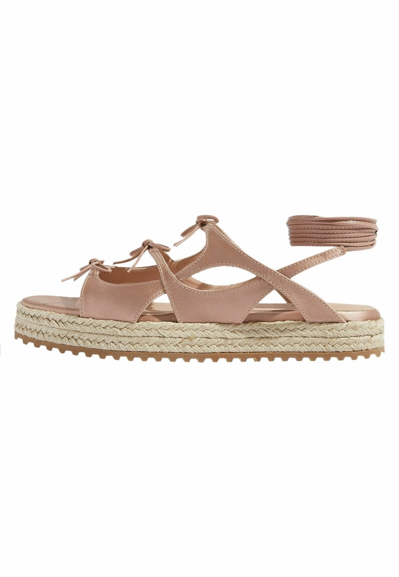 Sandale rose clair avec un design découpé, liens à l'avant et une plateforme en jute tressé. La semelle a une texture adhérente pour une meilleure traction.