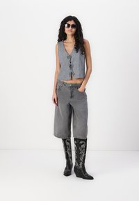 Μαύρο και άσπρο καρό κοντό γιλέκο με κλείσιμο κουμπιού, γκρι φαρδιά τζιν σορτς και μαύρες καμπυλωτές μπότες μέχρι το γόνατο με τακούνια wedge.