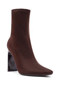 Botte de cheville marron avec une tige en tissu extensible et élégant, bout pointu et talon aiguille noir brillant. Détails de coutures sur les côtés.