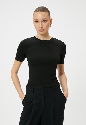 Zwarte ribbelige top met korte mouwen en een ronde halslijn, getailleerde pasvorm en zachte textuur, gecombineerd met hoge, op maat gemaakte broek.