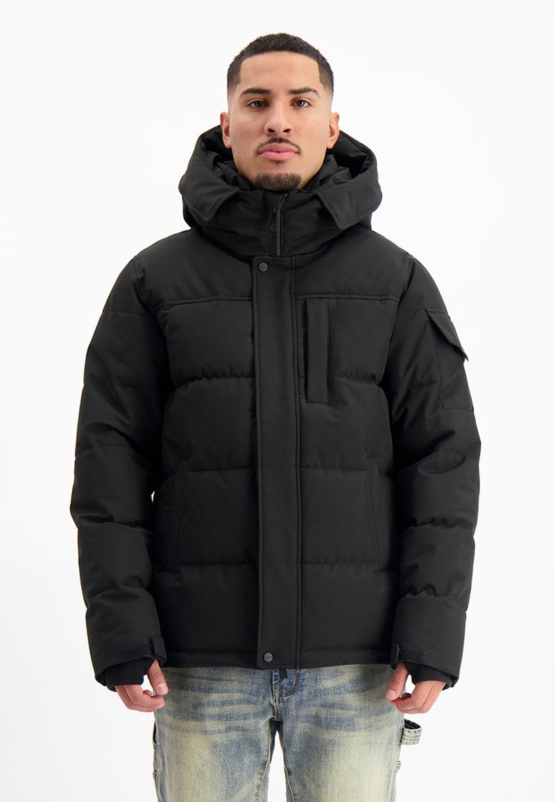 Zwarte pufferjack met een hoge kraag, ritssluiting aan de voorkant en drukknopen; heeft zijzakken en een textiel met zichtbare stiksels.