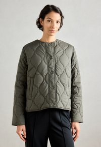 Olivengroene gewatteerde jas met een ronde halslijn, voorzien van ton-sur-ton stiksels en voorsluiting met knopen. Ontworpen met een slank figuur en een gestructureerd patroon.