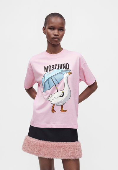 Γυναίκα που φοράει ροζ T-shirt Moschino με γραφικό μιας χήνας που κρατάει μια μπλε ομπρέλα και μαύρη φούστα με ροζ γούνινη επένδυση.
