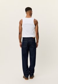 Άσπρο βαμβακερό αμάνικο τοπ, μπλε σκουρόχρωμο τζιν με κλασική εφαρμογή και πίσω τσέπες, με ραφές σε αντίθεση, συνδυασμένο με καφέ μπότες.