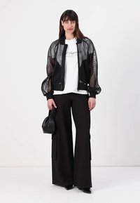 Black mesh bomber jacket over a white graphic T-shirt, paired with black wide-leg trousers. Accessories include a small black handbag.