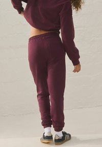 Bordeaux joggers med elastisk talje og opsmøgede tilminger, med en baglomme. Kombineret med sorte sneakers og hvide sokker.