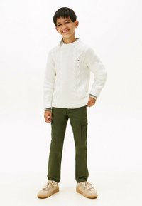 Hvit kabelstrikket genser med rund hals, kombinert med olivengrønne cargobukser og lysebeige joggesko. Flate sko med snøring.