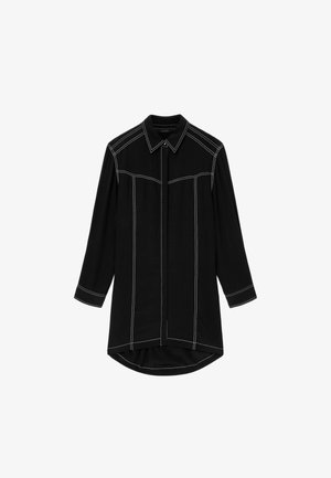 Zwarte overhemdjurk met lange mouwen, witte contrasterende stiksels, puntige kraag, verborgen knopen aan de voorkant en een iets afgeronde zoom die aan de achterkant langer is.