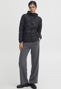 Zwarte gewatteerde jas met een capuchon en een ritssluiting aan de voorkant, gecombineerd met grijze wijde broek en zwarte schoenen. Eenvoudig ontwerp, zonder patronen of accenten.