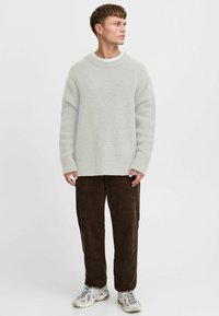 Light gray knitted sweater with a round neck, paired with brown corduroy pants and gray patterned sneakers. Simple design, relaxed fit.