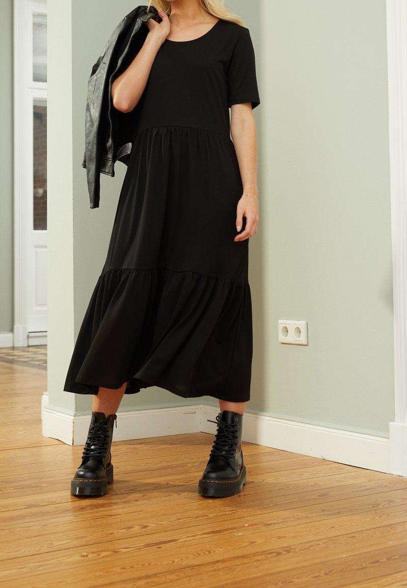 Robe noire à manches courtes avec une jupe à volants, fabriquée en matériau doux. Associée à des bottes noires à lacets avec une semelle épaisse.
