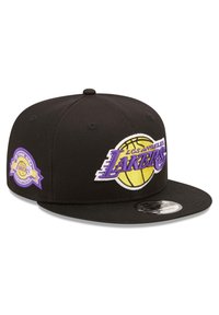 Gorra de béisbol negra con visera plana, con el logotipo bordado de "Los Angeles Lakers" en púrpura y amarillo, y un parche de campeonato en el lado.