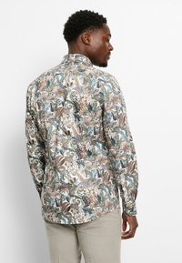 Long-sleeve shirt in patterned fabric featuring floral and paisley designs in blue, brown, and green, with a standard collar and button cuffs.