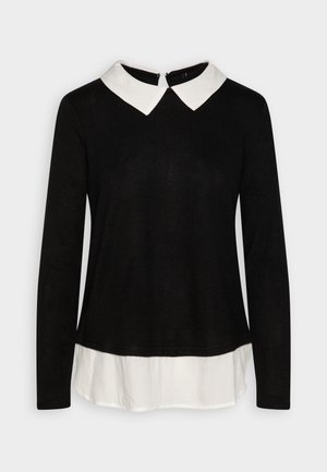 Haut noir à manches longues avec un col blanc, présentant une fermeture éclair discrète au dos et un look superposé avec une base de chemise blanche.