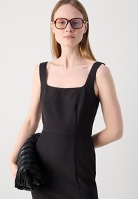Black fitted dress with wide shoulder straps, square neckline, and a smooth texture. Holding a black, pleated leather clutch.