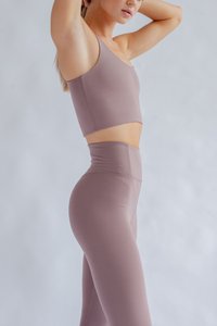 Mauve, pieglīts sporta krekliņš ar vienu plecu, saskaņots ar augsto vidukli legingiem tajā pašā krāsā, izgatavoti no elastīga auduma.