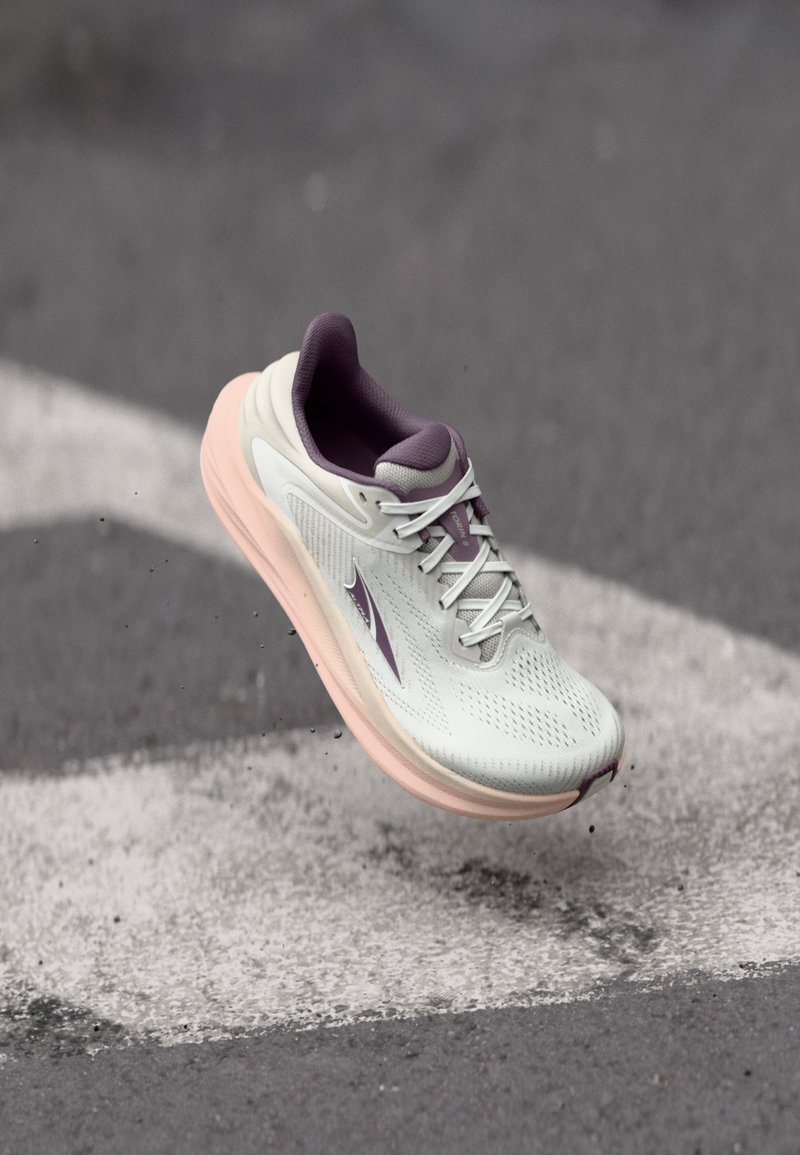 Chaussure de course avec une tige gris clair, des accents violets, un mesh respirant et une semelle rose rembourrée, présentée en l'air au-dessus d'une surface.
