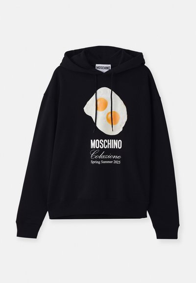Haut à capuche noir en coton avec un graphique d'œuf frit à deux jaunes, texte "MOSCHINO Colazione Printemps Été 2025" en dessous.