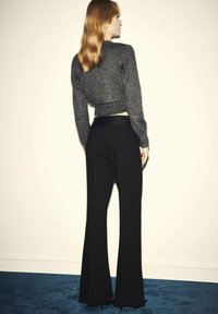 Suéter gris recortado con dobladillo acanalado combinado con pantalones de campana negros. Textura de tela suave, diseño minimalista, sin patrones ni acentos visibles.